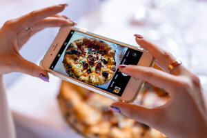 Eine Frau fotografiert mit ihrem Smartphone eine Pizza