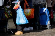 Menschen stehen in einer Warteschlange und haben Einkaufstüten in den Händen, neben ihnen stehen Einkaufstrolleys