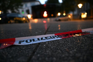 Im Halbdunkel ist ein Absperrband der Polizei erkennbar, im Hintergrund stehen Kerzen auf dem Asphalt