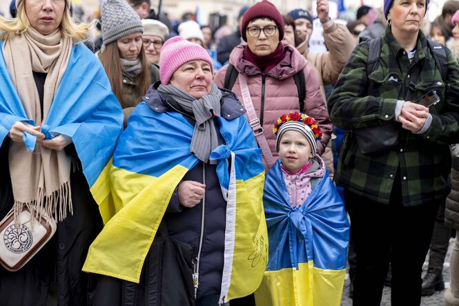 Eine Frau und ein Kind haben Fahne in den ukrainischen Nationalfarben um die SChultern gelegt. Sie stehen in einer Menschenmenge