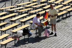 Ein Mann und eine Frau und Bierbänke. Sie halten deutsche und US-Fähnchen in den Händen