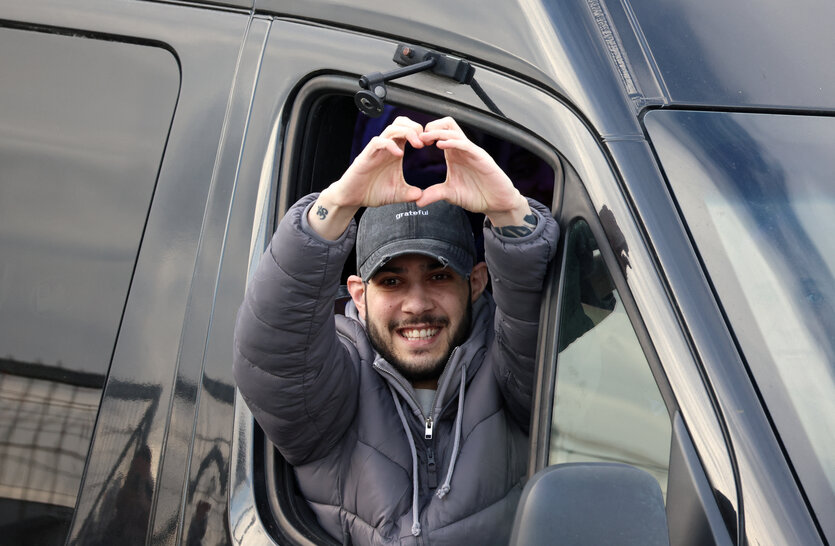 Ein Mann schaut aus dem Fenster eines Vans und formt lachend mit seinen Händen ein Herz