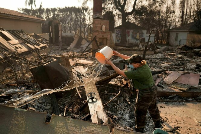 Nancy Belanger gießt Wasser auf das vom Feuer verwüstete Grundstück eines Nachbarn nach dem Palisades-Brand im Stadtteil Pacific Palisades von Los Angeles.