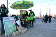 Infostand der Grünen mit grünem Sonnenschirm und einem Lastenfahrrad, Flyer liegen auf dem Boden