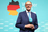 Friedrich Merz steht vor einem blauen Banner der CDU