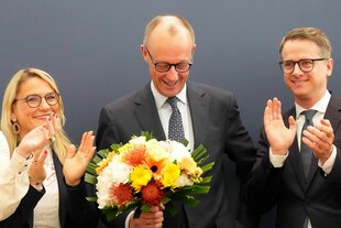 Freidrich merz bei einer Pressekonferenz mit Blumenstrauß.