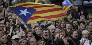 Eine Menschenmenge. Ein Mann hält eine Flagge Kataloniens