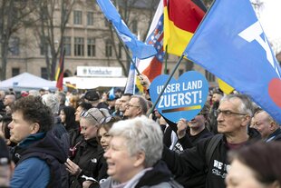 Teilnehmer einer Kundgebung in Erfurt, Menschen unterschiedlichen Alters schwingen Deutschland- und AfD-Flaggen und einer hält ddas Plakat hoch: Unser Land zuerst