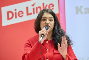 Cansu Özdemir mit einem Mikrofon vor einem Schriftzug "Die Linke"