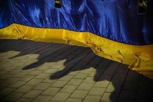 Eine ukrainische Flagge auf einer Demonstration mit den Schatten der Demonstrant*innen