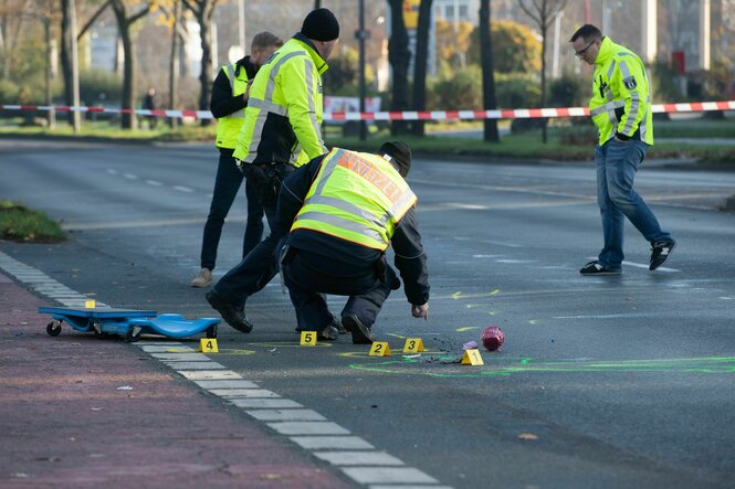 Polizisten in Warnwesten sichern Spuren auf einer mit rot-weißem Flatterband abgesperrten Straße