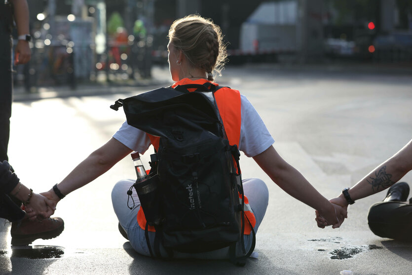 Mensch im Schneidersitz auf einer Straße, Hand in Hand mit weiteren