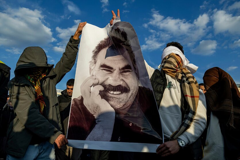 Zwei mit Schal vermummte Personen halten ein Bild von Öcalan mit Siegespose empor