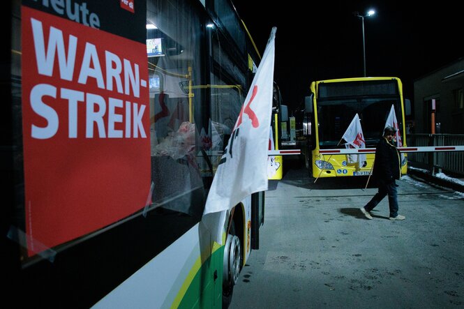 Eine Frau geht an Bussen der Berliner Verkehrsbetriebe BVG mit Fahnen der Gewerkschaft Verdi und dem Schild «Heute Warnstreik» im Betriebshof Lichtenberg entlang.