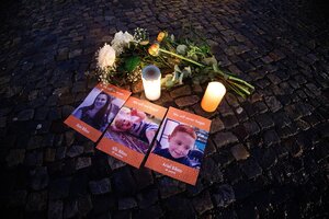 Kerzen, Blumen und Fotos einer Frau und zweier Kinder liegen auf feuchtem Asphalt