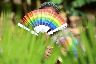 Jemand versteckt sich hinter einem Fächer in Regenbogenfarben