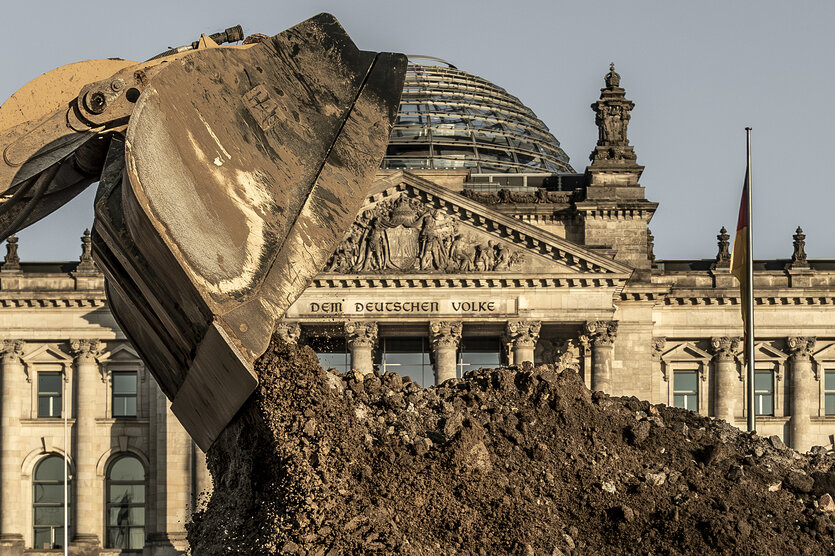 Ein Bagger arbeitet vor dem Reichstagsgebäude an einem großen Erdhaufen