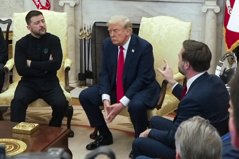 Selenskyj und Trump sitzen in weißen Sesseln und sehen unzufrieden aus. Rechts von ihnen sitzt auf einer Couch JD Vance und gestikuliert