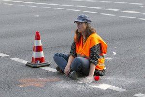 Eine Person sitzt bei einer Straßenblockade auf der Straße.