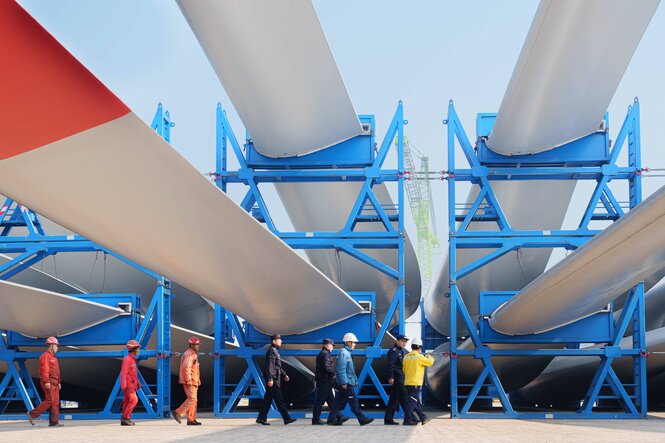 Chinesische Arbeiter laufen vor rot-weißen Windturbinenblätter, die auf blauen Gestellen gelagert sind