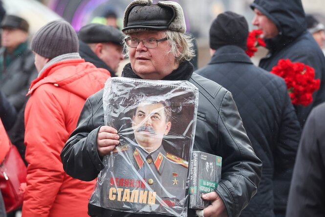 Ein Mann mit einer Fellmütze hält ein Portrait von Josef Stalin in den Händen