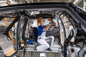 Eine Frau Montiert Teile an eine Karosserie eines Autos in einer Werkshalle von VW