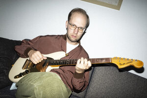 Albrecht Schrader auf dem Sofa, eine Gitarre im Anschlag.