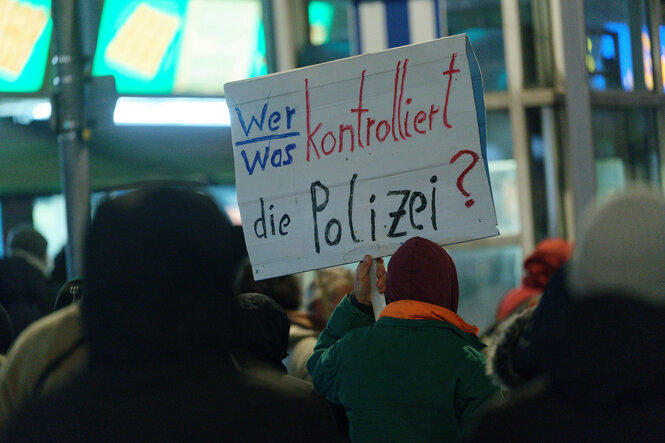 Demonstranten halten ein Schild hoch: "Wer/ was kontrolliert die Polizei?"