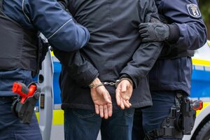 Zwei Hände in Handschellen hinter dem Rücken, links und rechts ein Polizist