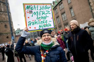 "Nicht jeder Merz bringt Frühlingsgefühle" steht auf dem SChild, das eine lachende Demonstrantin über den Kopf hält