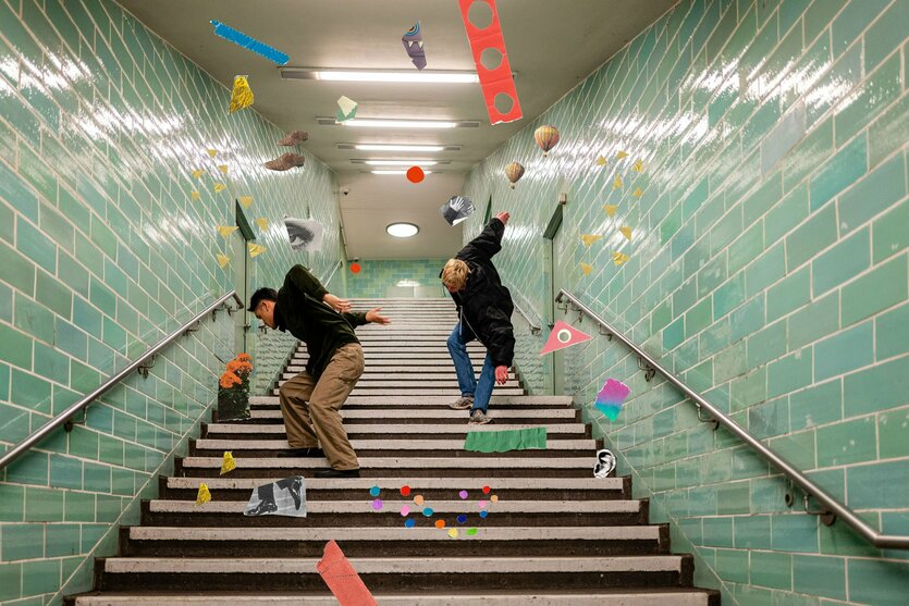 Zwei Tänzer laufen inmitten bunter Formen rückwärts auf einer Treppe