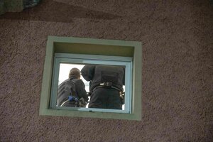 Durch ein kleines Fenster sind zwei Ermittler der Polizei zu sehen