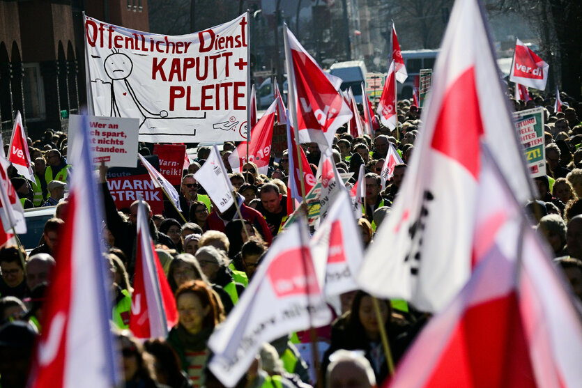 Teilnehmer halten während eines Verdi-Warnstreiks von Pflegepersonal am Charité Campus Virchow-Klinikum Schilder und Fahnen hoch, auf denen unteranderem steht: „Öffentlicher Dienst kaputt + pleite“