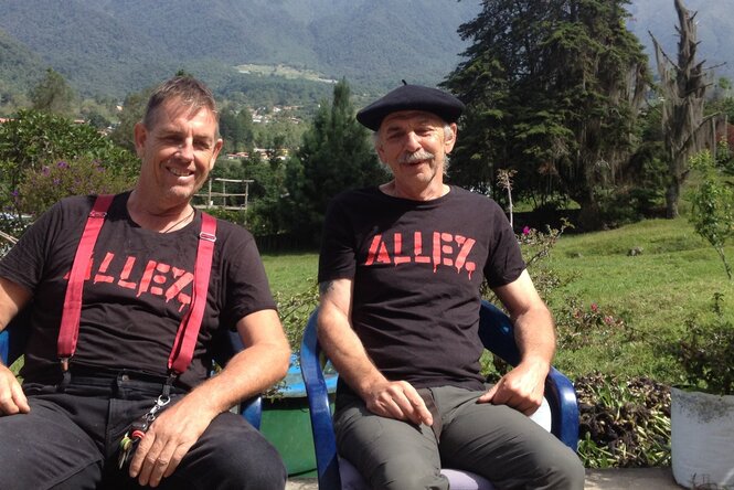 Thomas Walter und Peter Krauth sitzen im Freien und schauen in die Kamera. Auf ihren T-Shirts steht rot auf schwarz: "Allez"