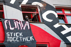 Ein „Flinta stick together“-Transparent hängt an einem Haus, eine Frau wirft Konfetti aus dem Fenster