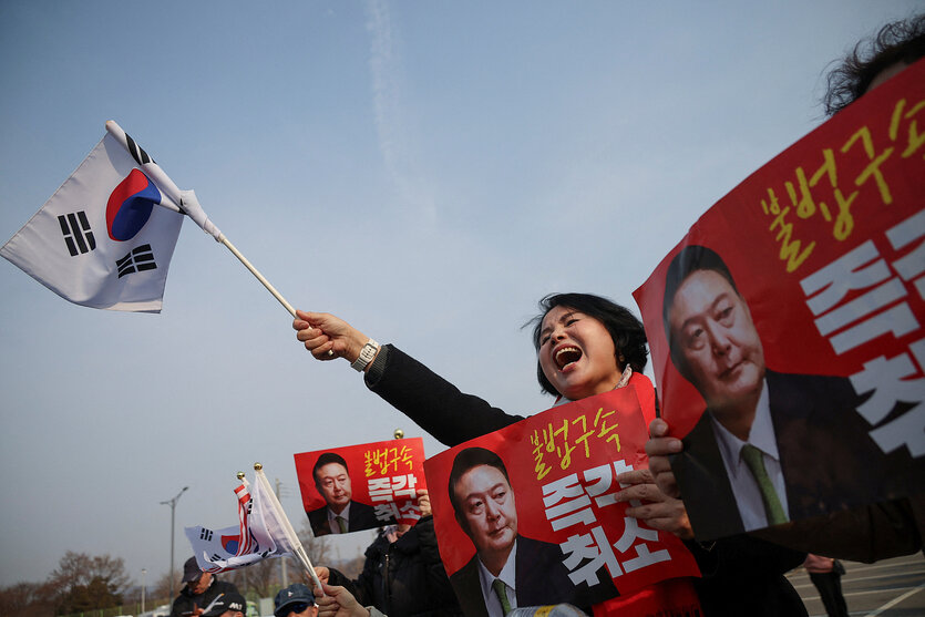 Eine Frau schwenkt eine koreanische Fahne, außerdem sind Plakate mit dem Konterfei des abgesetzten Präsidenten Yoon Suk Yeol zu sehen