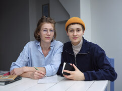 Hannah Elias (links) und Leyb-Anouk Elias (rechts) sitzen an einem Tisch und schauen in die Kamera.