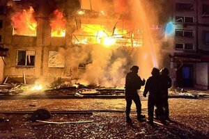 Feuerwehrmänner vor einem lichterloh brennenden Gebäude in der Nacht