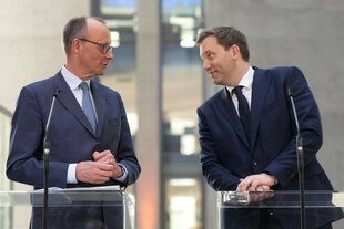 Lars Klingeil lehnt sich am Rednerpult zu Friedrich Merz