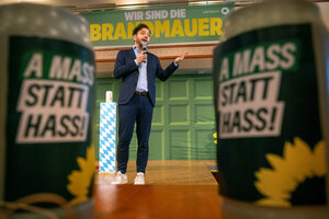 Mann mit Mikrofon zwischen Bierkrügen mit der Aufschrift 