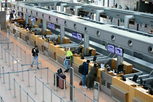 Vor den Check-In-Schaltern des Hamburger Flughafens stehen vier Personen.