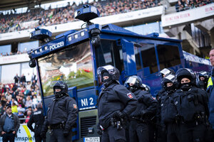 Polizisten stehen neben einem Wasserwerfer vor der Zuschauertribüne