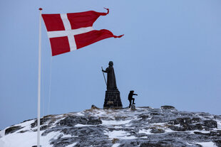 Ein Mann geht, während die dänische Flagge im Wind flattert, neben der Hans-Egede-Statue in Nuuk, Grönland