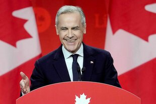 Porträt eines lächelnden Mark Carney am Rednerpult, der vor einer kanadischen Flagge eine Rede hält