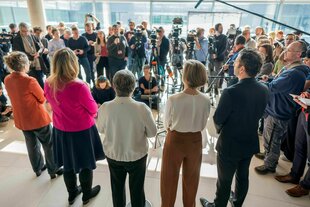 Verschiedene Personen stehen in einer Reihe und sprechen mit Vertretern der Presse