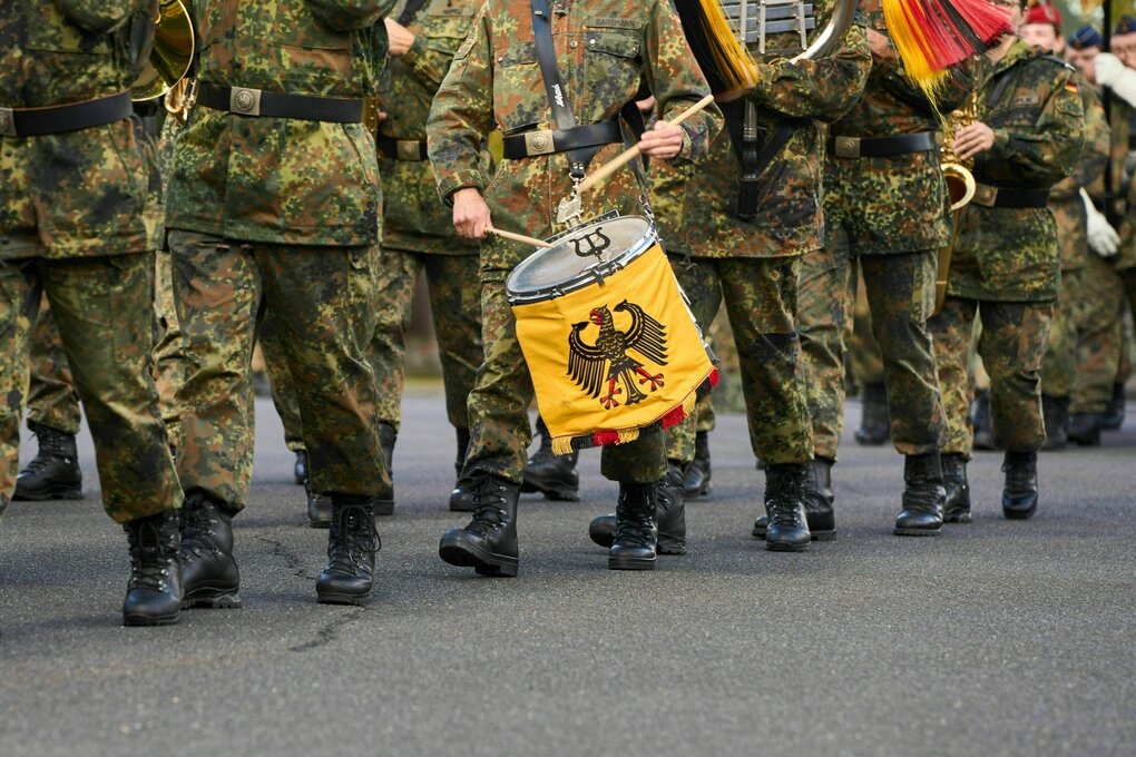 Bundeswehrsoldaten marschieren in Formation, ein Trommler trägt eine Trommel mit dem deutschen Bundesadler. Sie tragen die typische Camouflage-Uniform und Kampfstiefel. Musikkorps bei einer militärischen Zeremonie