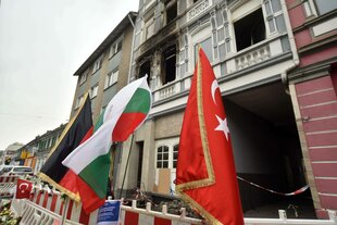 Drei Flaggen sind vor einem ausgebrannten Haus zu sehen