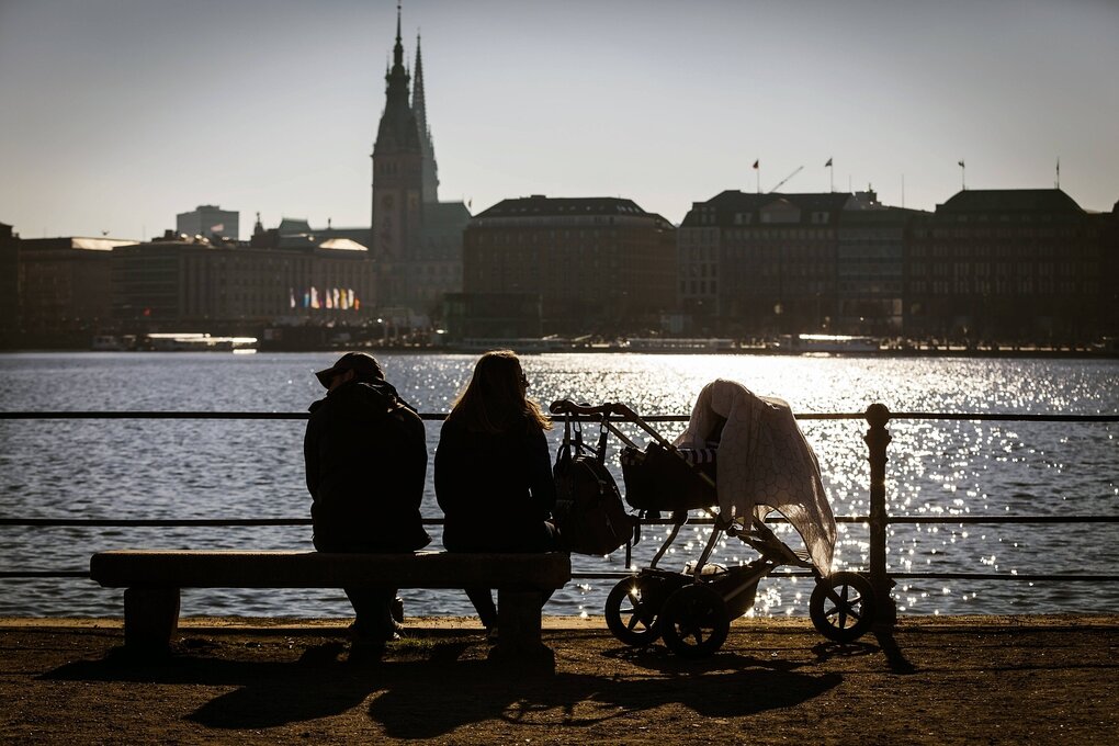 Silhoeutte eines Paars mit Kinderwagen vor der Kulisse der Hamburger Außenalster