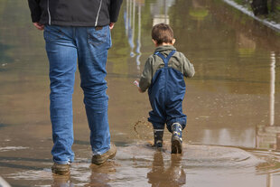 Kind in Regensachen watet in erwachsener Begleitung durch Hochwasser