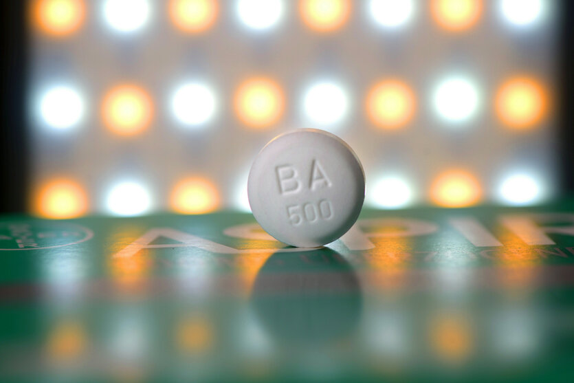 Eine weiße Aspirin Tablette vor angeleuchtet von gelben und weißen Lichtern im Hintergrund